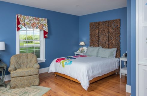 Pretty blue bedroom with a window, armchair and interesting wooden bed made up with a striking flowered duvet.