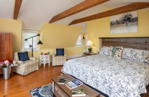 Yellow bedroom with wooden ceiling beams, modern wooden bed, seating area and a wooden screen.