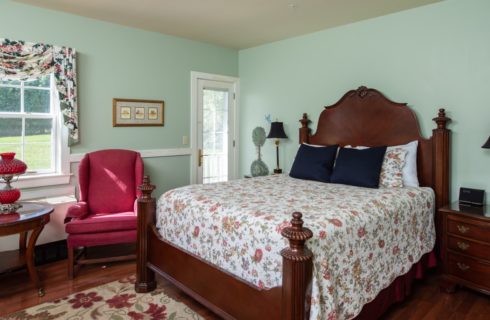 Bedroom painted pale green with dark Federal-style furniture and red and cream floor rug and coverlet on bed.